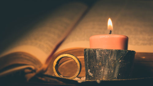 Close-up of illuminated candle in container by book