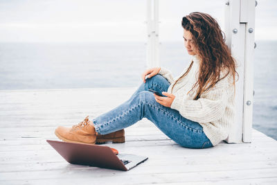 Woman looking at laptop while sitting on pier