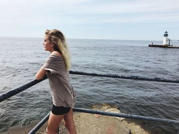 Side view of woman leaning on railing while standing against sea