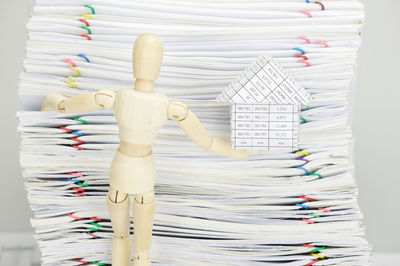 Close-up of wooden figurine holding model house against stacked files over gray background