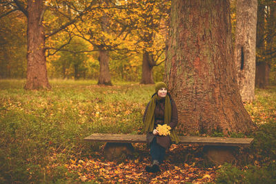 Women sits at bench near big tree in autumn forest