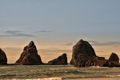 Rock formations in sea against sky during sunset