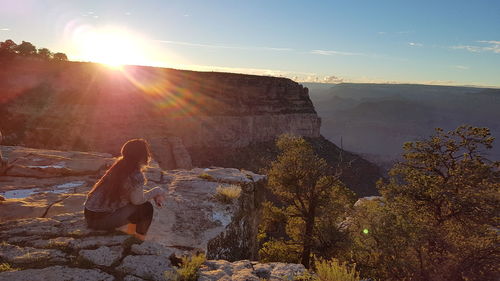 Woman sitting on rock looking at mountain against sky