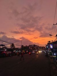 Cars on street against sky at sunset