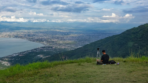 Man sitting on mountain against sky