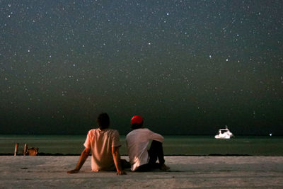 Two people sitting on beach looking at stars