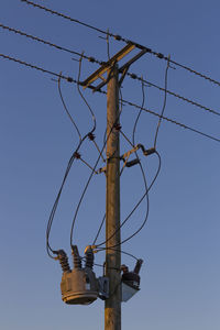 Low angle view of electricity pylon against clear blue sky