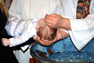 Midsection of priest pouring water on baby boy head