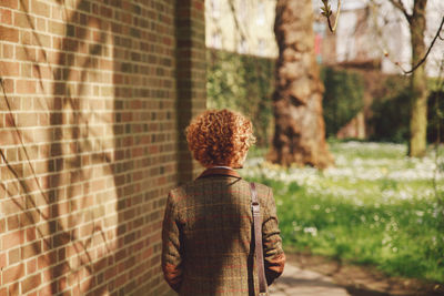 Rear view of woman on footpath by brick wall