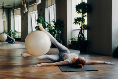 Full length of woman exercising with ball while lying down at gym
