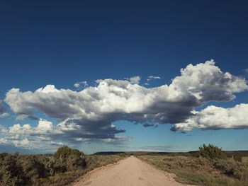 Dirt road amidst landscape against sky