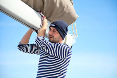 Low angle view of man holding canvas while standing against blue sky