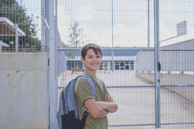 Portrait of smiling boy with arms crossed standing against school