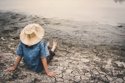 Rear view of girl sitting by pond on drought field