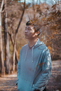 Young man looking away while standing by plants