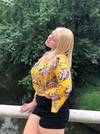 Young woman standing by railing against trees