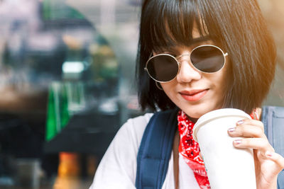 Young woman wearing sunglasses drinking coffee in city