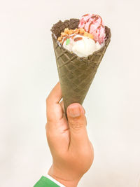 Close-up of hand holding ice cream cone against white background