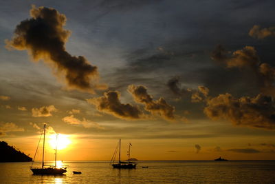 Silhouette sailboats in sea against dramatic sky during sunset