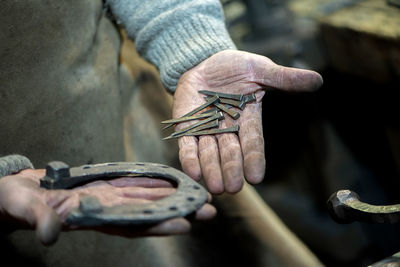 Close-up a dirty blacksmith's hand holds a horse's horseshoe and nails