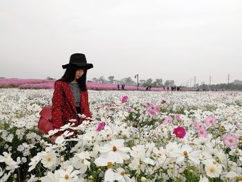 Woman standing amidst flowers on field against sky