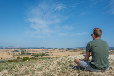 Rear view of man sitting on field against blue sky