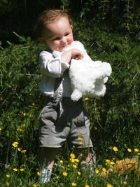 Smiling baby boy holding stuffed toy while standing on field