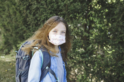Portrait of girl wearing mask while standing with backpack