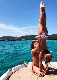 Girl helping sibling to do handstand on yacht 