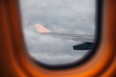 Airplane wing against sky seen through glass window