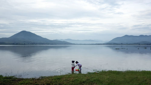 People standing by lake against sky