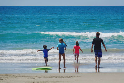 Rear view of daughters with father walking at beach