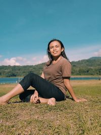 Portrait of young woman sitting on field against sky