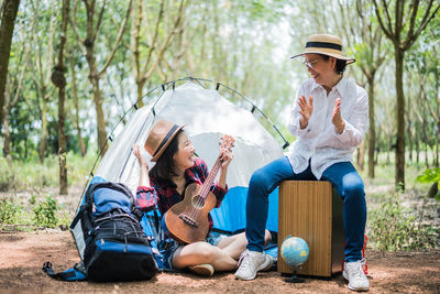 Smiling women sitting with ukulele at campsite in forest