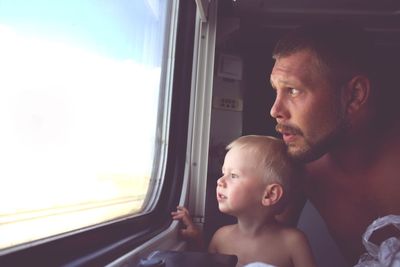 Father and son looking through window while sitting in train