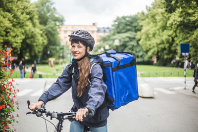 Portrait of smiling food delivery woman with bicycle on street in city