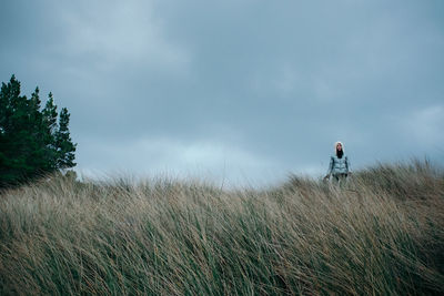 Woman walking on grassy field against cloudy sky