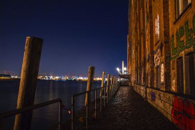 Illuminated city by sea against clear sky at night