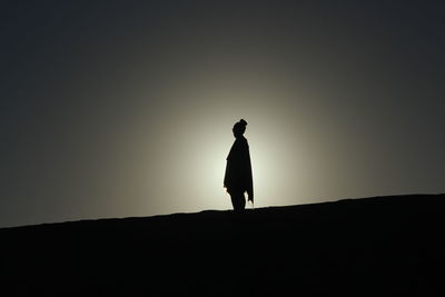 Silhouette woman standing on landscape against sky during sunset