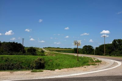 Empty road amidst field against sky