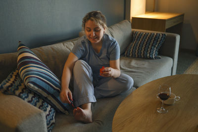 Portrait of young woman using mobile phone while sitting on sofa at home