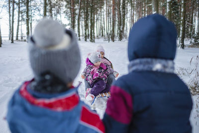 Happy friends have fun in wonderland, little two boy pulls a sledge with sisters across forest