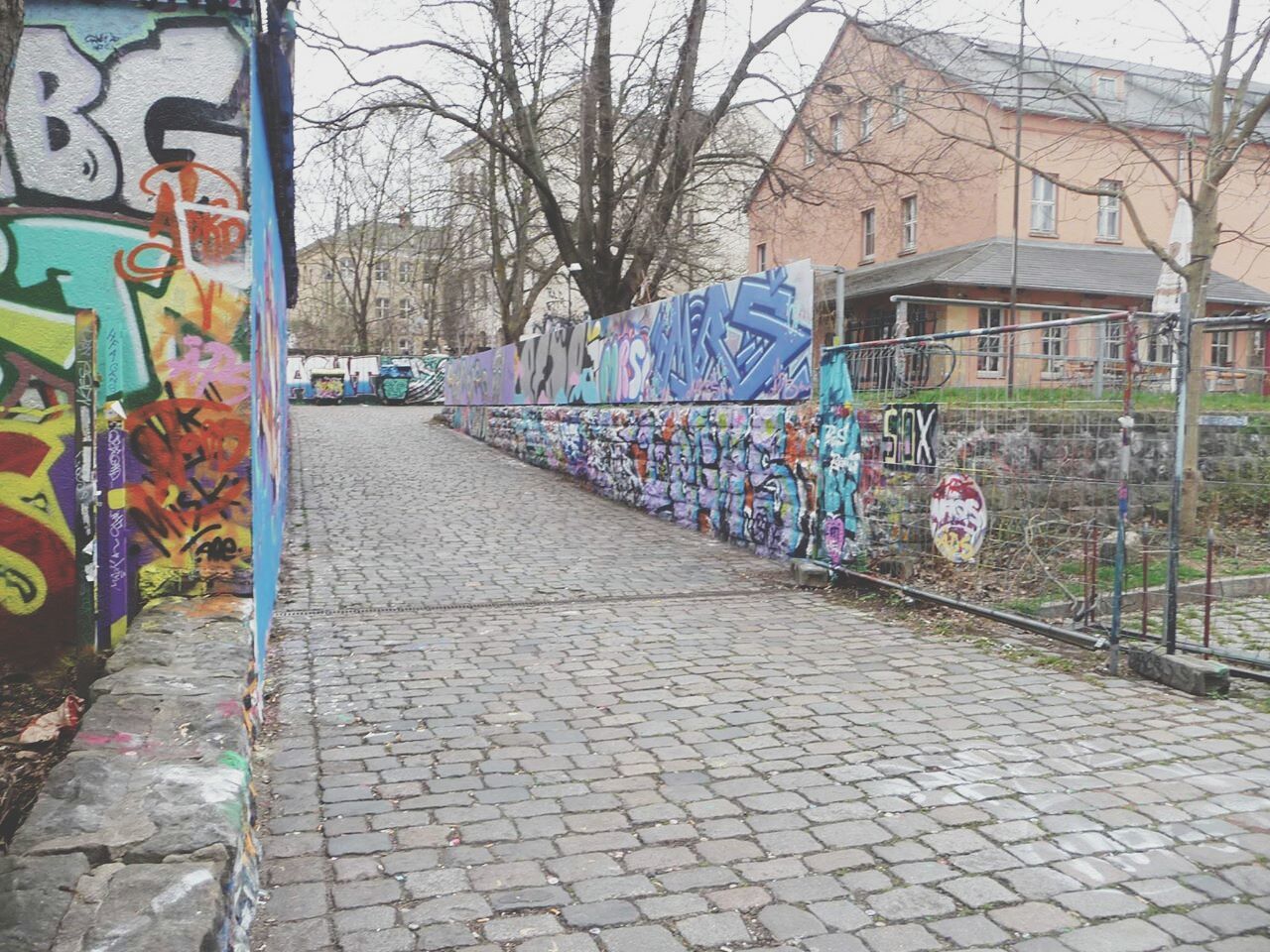 building exterior, architecture, built structure, graffiti, cobblestone, street, the way forward, city, art and craft, sidewalk, art, multi colored, paving stone, transportation, footpath, wall - building feature, day, outdoors, creativity, tree