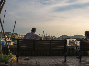 Rear view of man sitting on harbor against sky