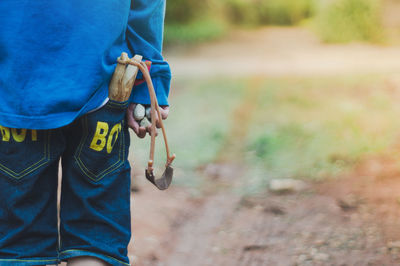 Rear view of boy with slingshot and rocks standing on field