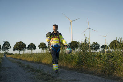 Technician walking on field path at a wind farm with climbing equipment