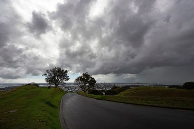 Empty road on field against cloudy sky