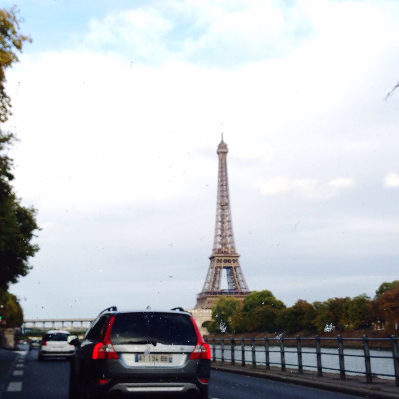 transportation, eiffel tower, sky, built structure, architecture, car, tower, tree, famous place, travel destinations, road, travel, land vehicle, international landmark, metal, tourism, capital cities, tall - high, cloud - sky, mode of transport