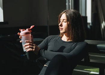 Portrait of resting young brunette woman in sport active wear drinking water in the fitness club