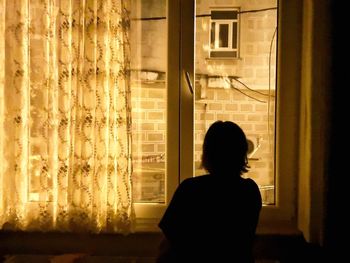 Rear view of silhouette man looking through window